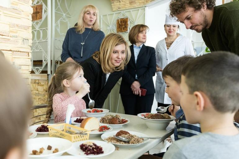 Елена Зеленская возле стола с детьми которые кушают