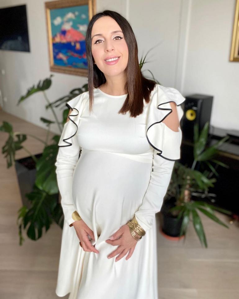 Беременная Джамала в белом платье стоит в комнате