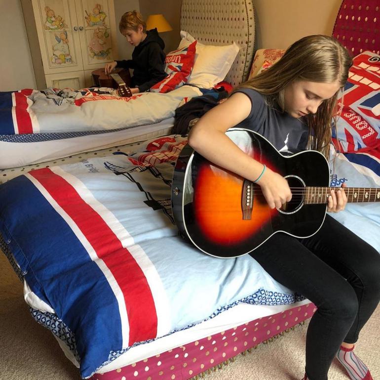 Нева сидит на кровати играет на гитаре