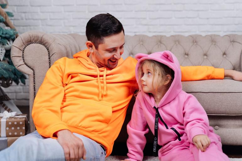 Андрей Шабанов с ярком свитшоте сидит с дочерью на диване