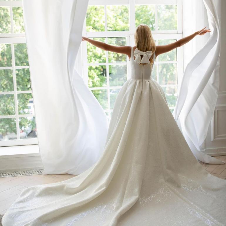 Ірина Федишин стоїть біля вікна у весільній сукні