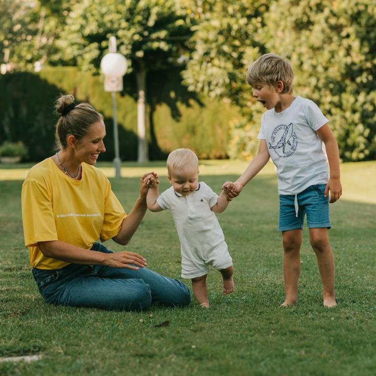 Катя Осадча сидить на газоні з синами